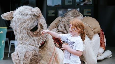 Young girl with red hair pats a giant camel puppet